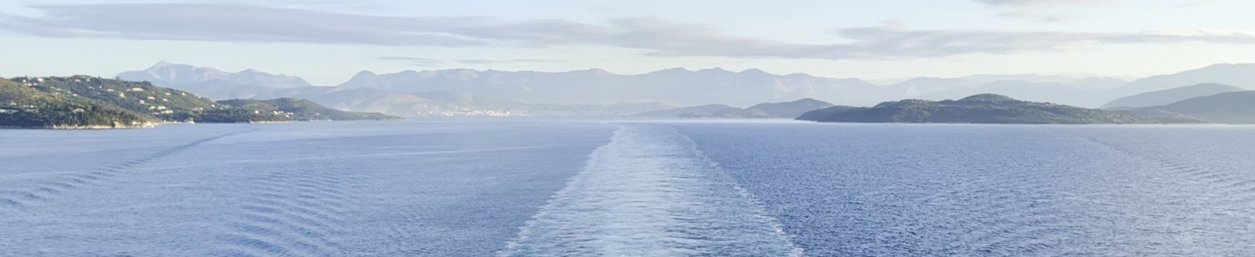 Kielzog van een schip op een kalme zee voor een kust met bergen
